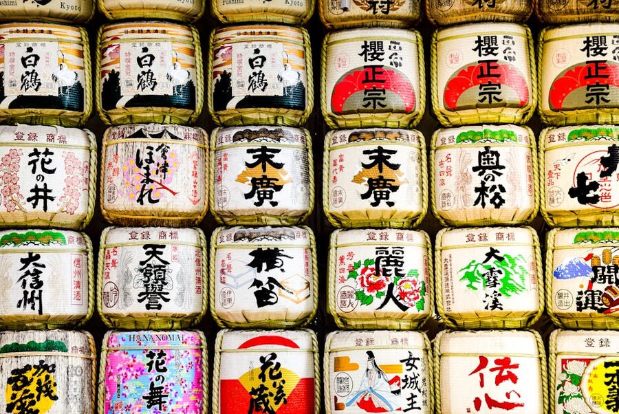 Wall of brightly decorated sake barrels stacked along the path at Meiji Jingu