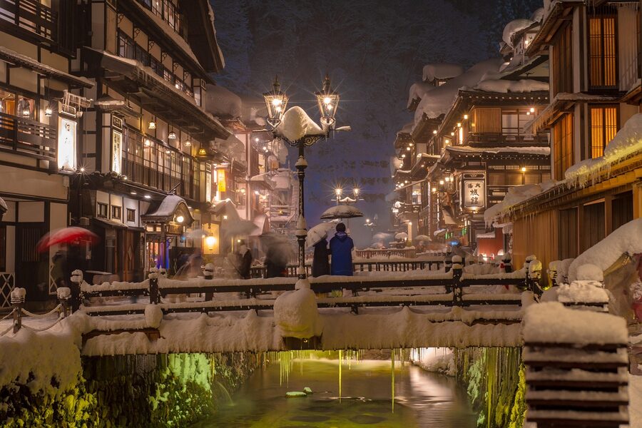 Footbridge in a snowy Japanese onsen town lit up at night